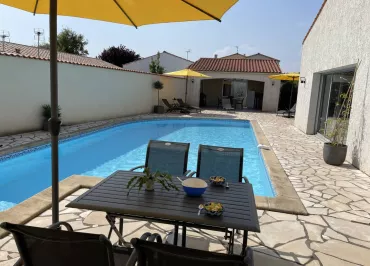 La terrasse avec piscine découverte, un salon de jardin métallique et un parasol sur pied.