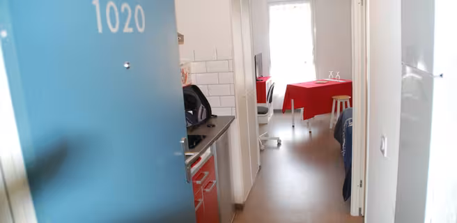 La porte d'entrée bleu ouverte sur le studio, on voit la petite kitchenette et la salle à manger.